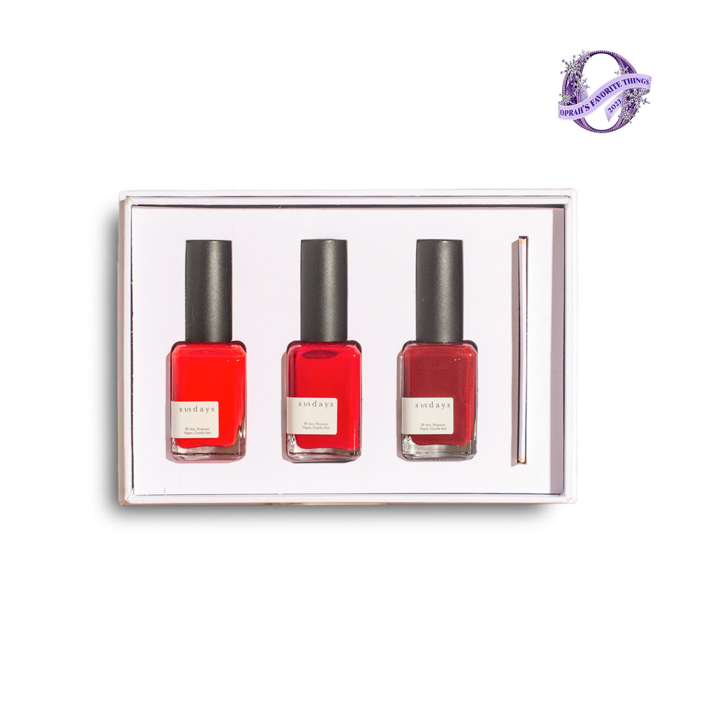 A gift box containing three bottles of red sundays studio nail polish and a pen, presented on a white background.